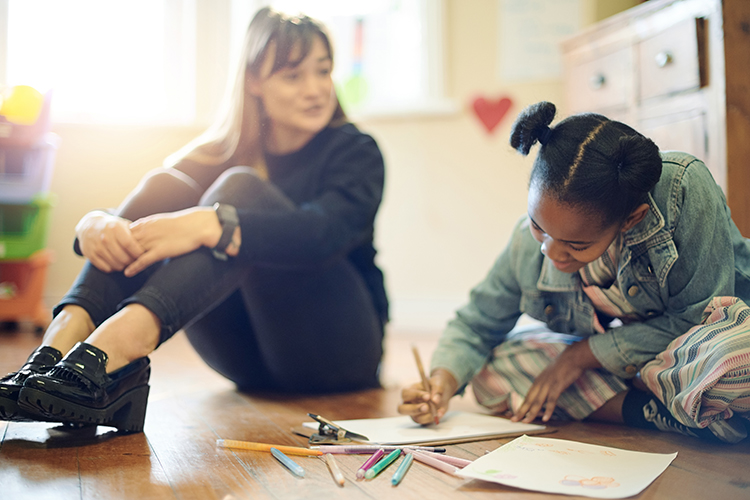 A woman sitting next to a child that's drawing